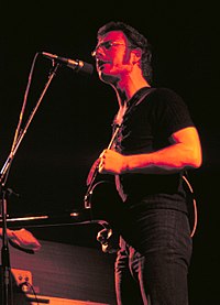 A red tinted image of a young man, Robert Fripp, playing guitar