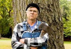 Man-holding-an-axe-leaning-against-a-tree.jpg